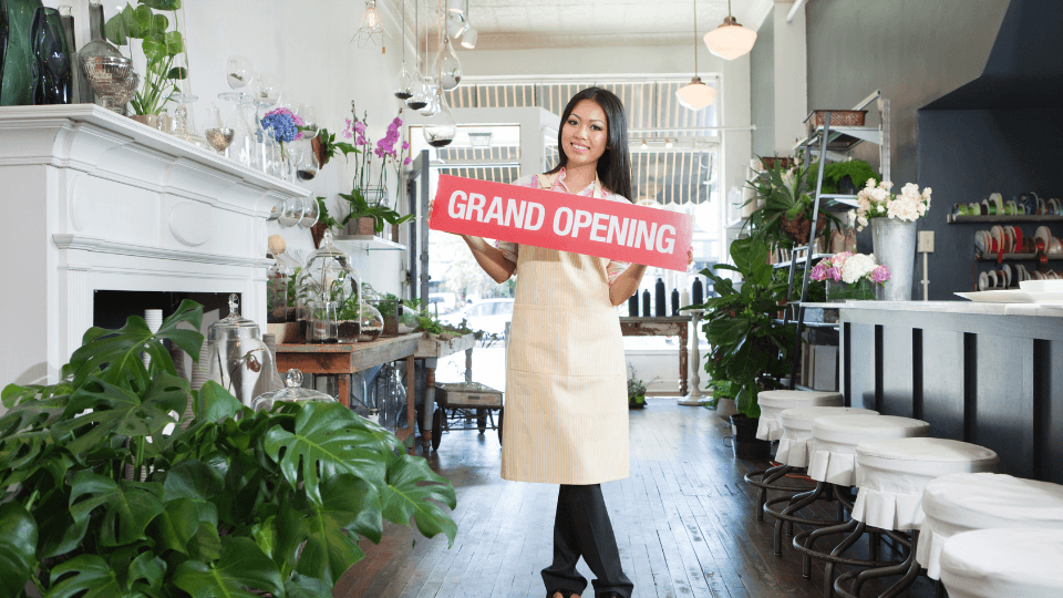 Image of a female business owner holding a grand opening sign